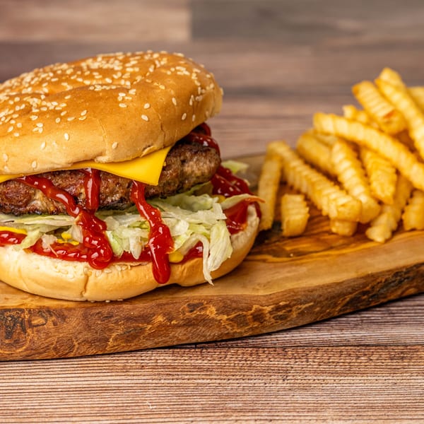 Cheeseburger with lettuce, ketchup, and mustard, served with crinkle-cut fries on a wooden board.