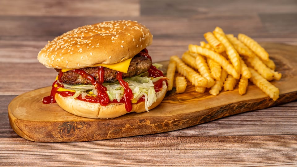 Cheeseburger with lettuce, ketchup, and mustard, served with crinkle-cut fries on a wooden board.