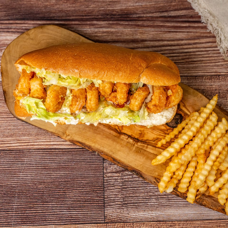 A shrimp po'boy sandwich with lettuce and fries on a wooden board.