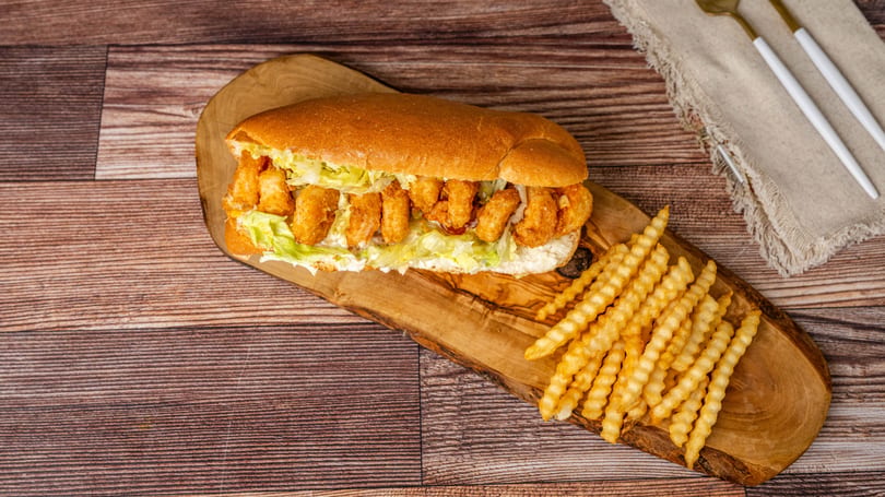 A shrimp po'boy sandwich with lettuce and fries on a wooden board.