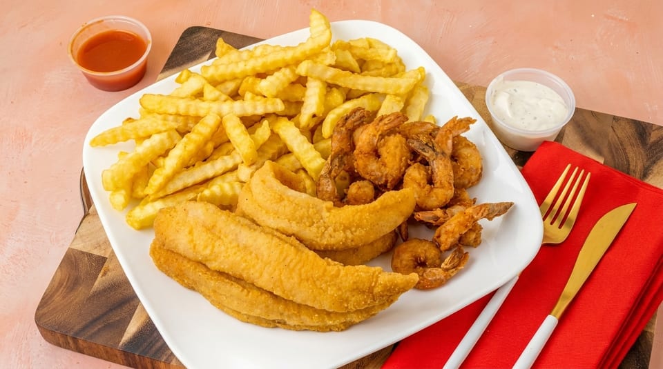 Fried fish fillets, shrimp, and crinkle-cut fries with ketchup and tartar sauce on a white plate.