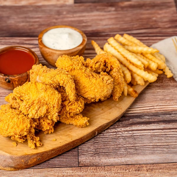Crispy fried chicken tenders and crinkle-cut fries on a wooden board with dipping sauces.