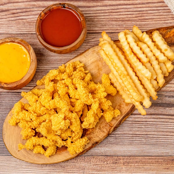 Crispy fried chicken pieces and crinkle-cut fries on a wooden board with ketchup and cheese sauce.