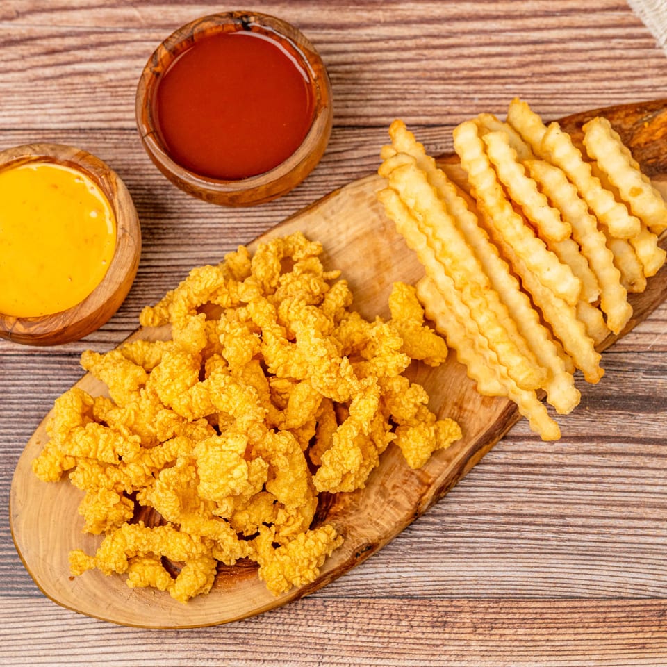 Crispy fried chicken pieces and crinkle-cut fries on a wooden board with ketchup and cheese sauce.