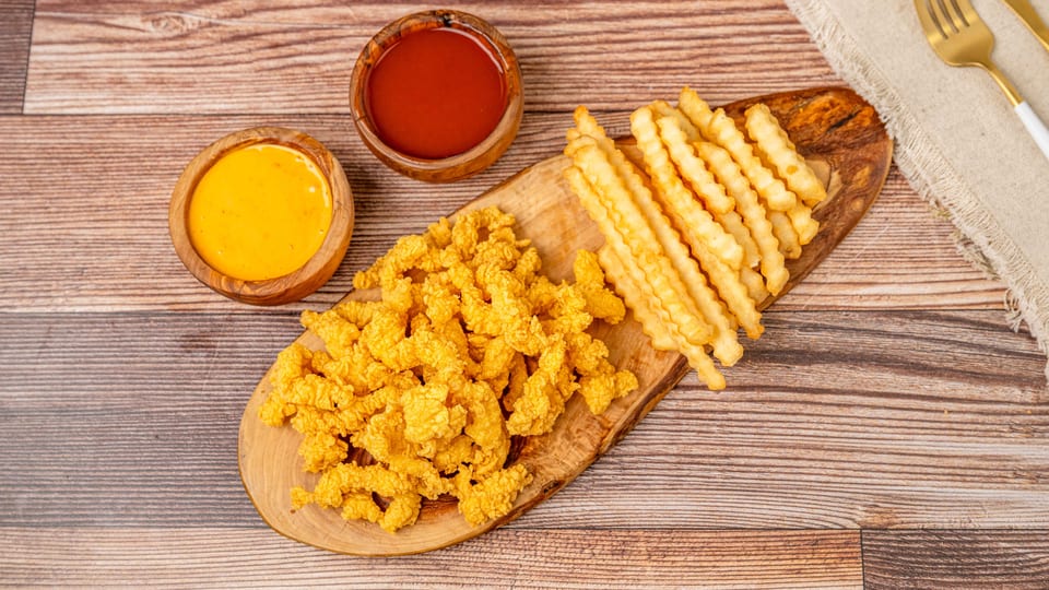 Crispy fried chicken pieces and crinkle-cut fries on a wooden board with ketchup and cheese sauce.