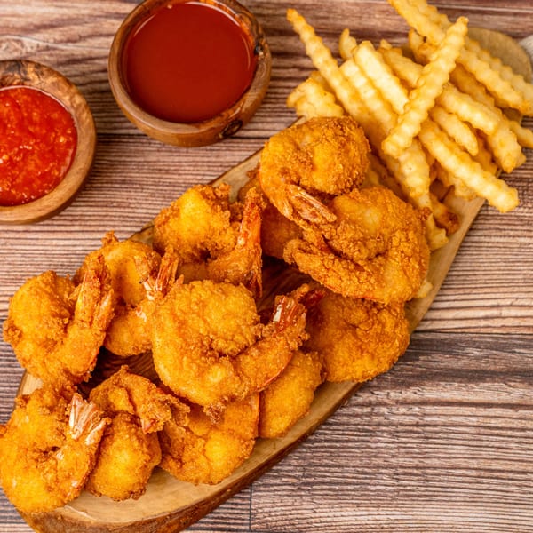 Crispy fried shrimp and crinkle-cut fries on a wooden board, with two bowls of dipping sauce.