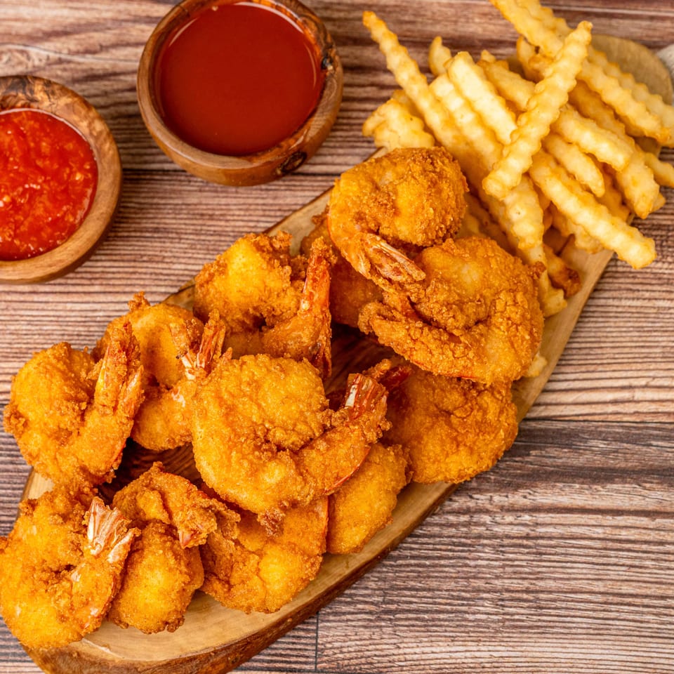 Crispy fried shrimp and crinkle-cut fries on a wooden board, with two bowls of dipping sauce.