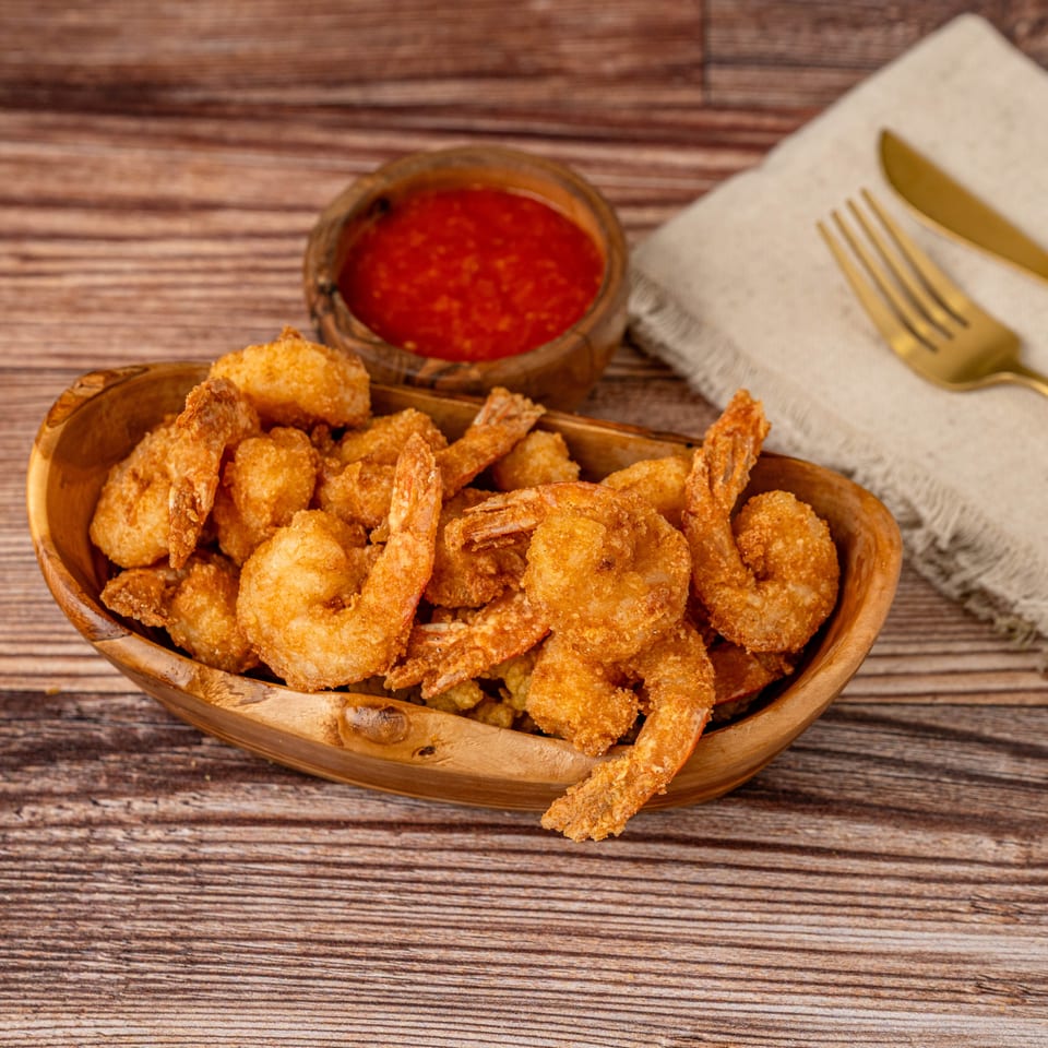 Golden fried shrimp in a wooden bowl, with red dipping sauce and gold cutlery on a napkin.
