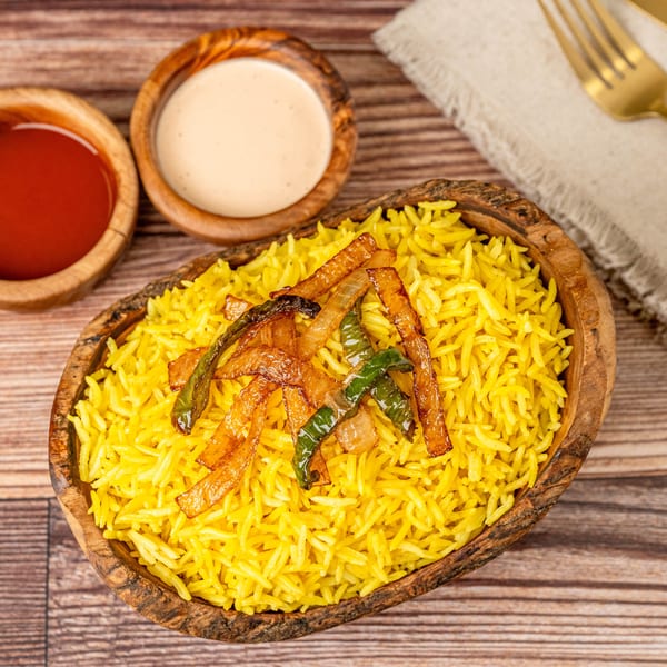 Yellow rice topped with fried onions and green peppers, with two dipping sauces and cutlery.