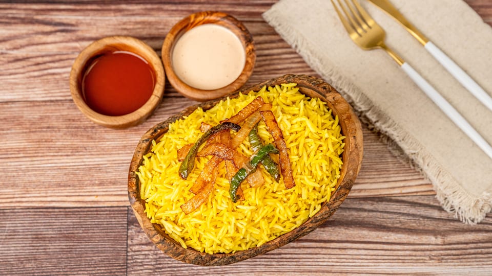 Yellow rice topped with fried onions and green peppers, with two dipping sauces and cutlery.