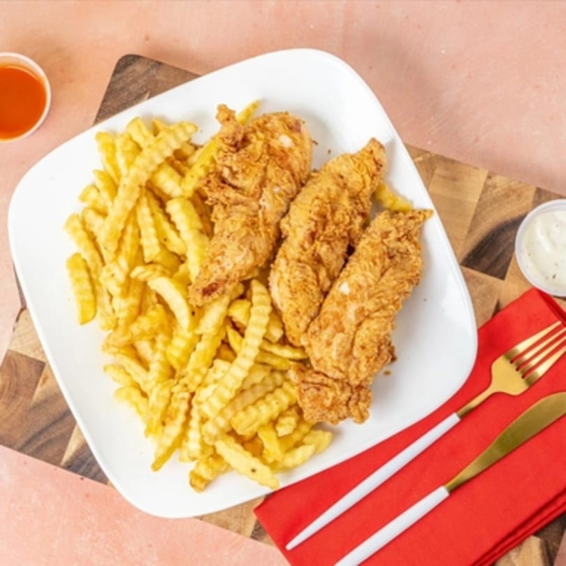 Three crispy fried chicken tenders and crinkle-cut fries on a white plate with dipping sauces.