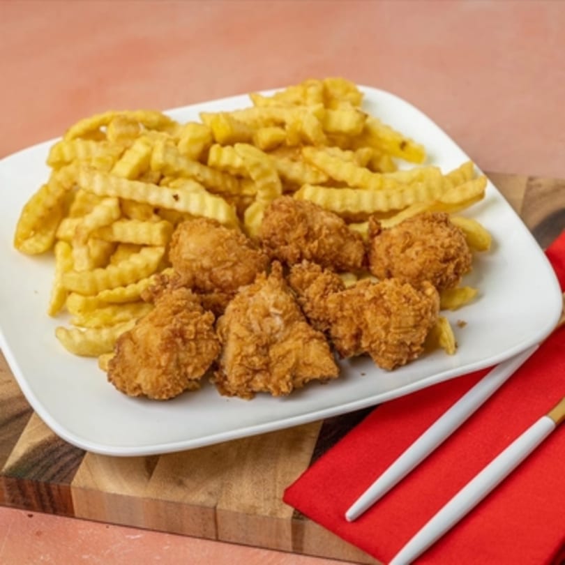A white plate of golden-brown fried chicken pieces and crinkle-cut fries, with chopsticks on a red napkin.